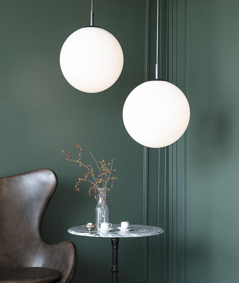 Dark green painted wall with two hanging white glass pendants above a marble table