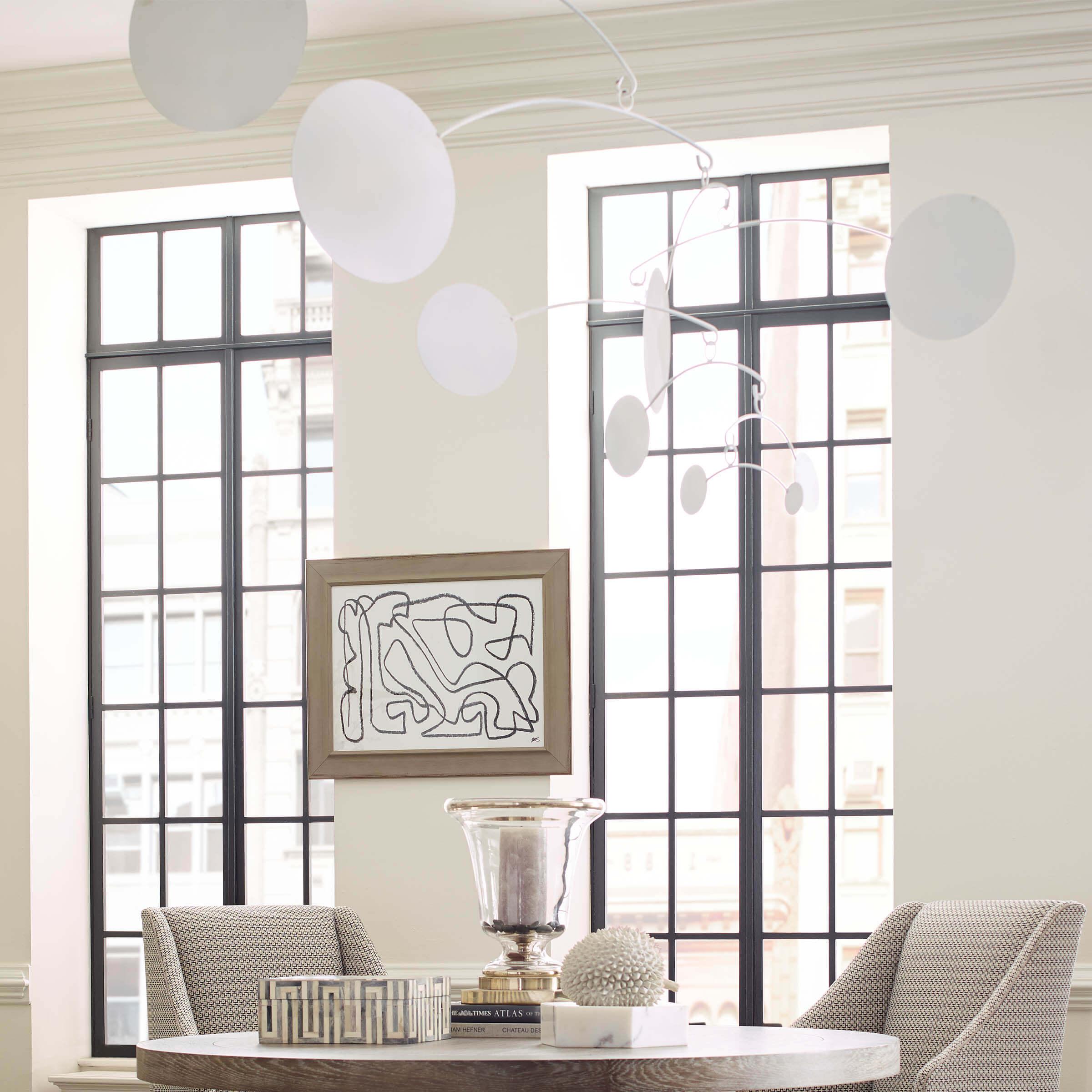 Luxury apartment dining room with wood table, chairs, a photo, and a hanging mobile made of white disks and swinging arms