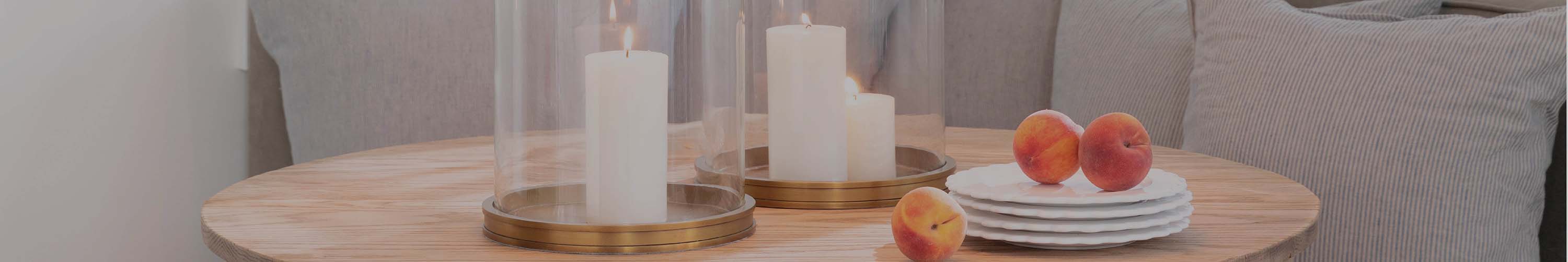 Two glass and brass hurricane sholding candles on a wood table