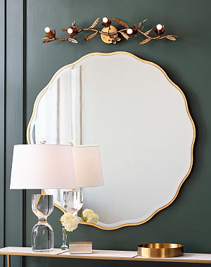 Large gold rimmed wall mirror with a natural brass sconce above it