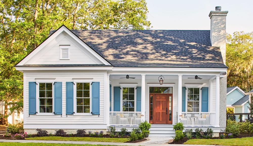 Southern styled home with blue shutters, green grass and shrubs, and a natural wooden door