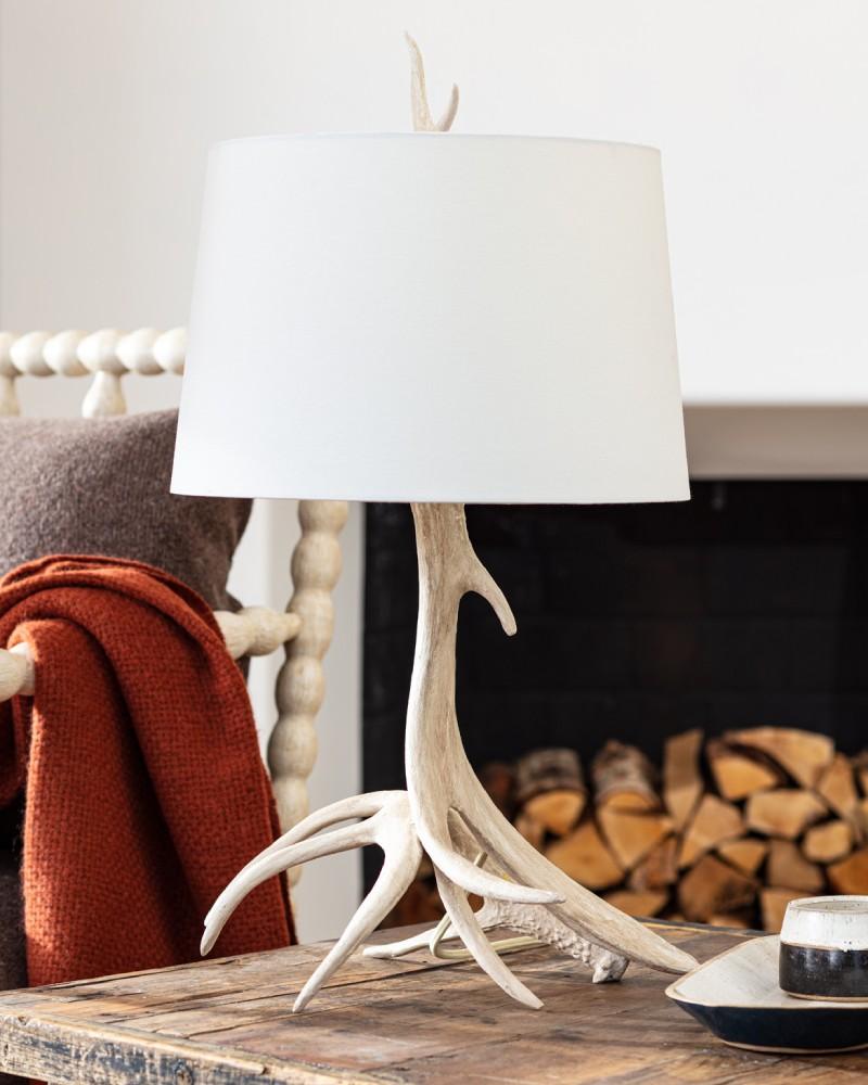 Rustic southern decor antler lamp with a white shade on a wooden side table