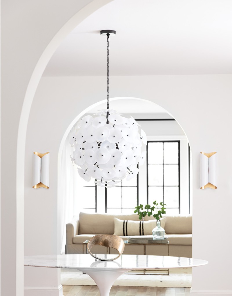 Home entryway with a glass table, a white flowered chandelier, white gold sconces, and a brown couch