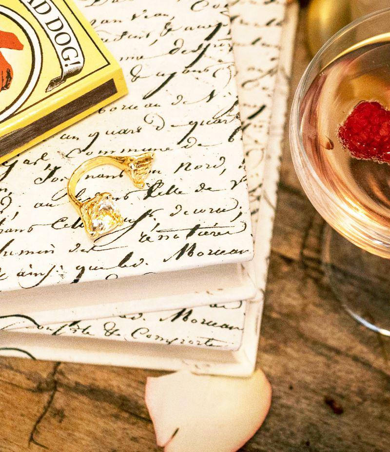 Wooden table with a cocktail glass, white books, and a gold ring