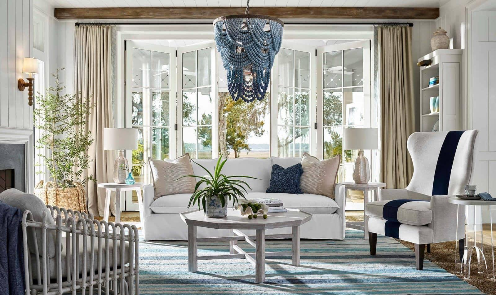 A coastal living room with a white couch, blue chandelier and wood coffee table