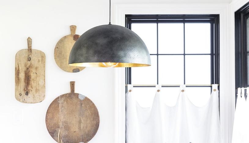 A black metal ceiling light with a window and a wall of cutting boards behind it