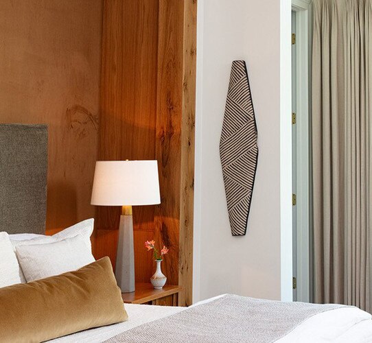 Long shield on a wall next to a table lamp and bed