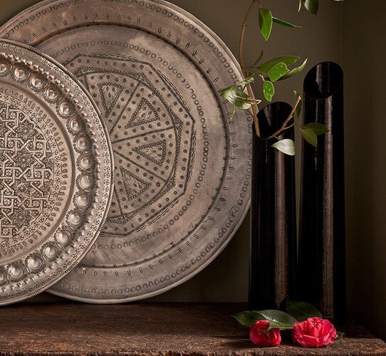 Black vases with branches in them next to antique silver plates