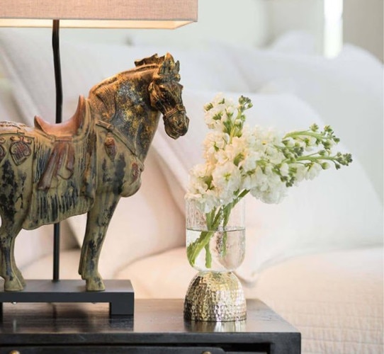 Metal horse lamp on a bedside table next to a vase of flowers