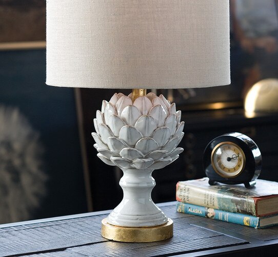 White ceramic artichoke lamp with gold base on a rustic wooden side table