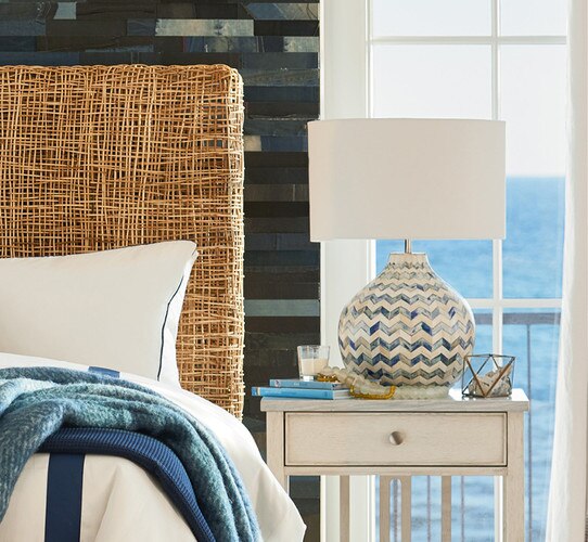 Circular bone table lamp on a white bedside table in front of a window