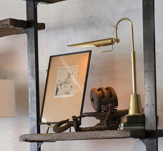 Slim brass task lamp on a wooden shelf next to a vintage metal pulley