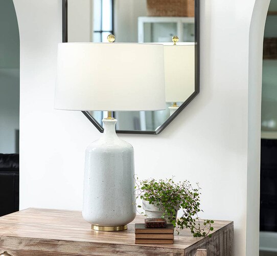 Gray ceramic table lamp on a side table under a black mirror