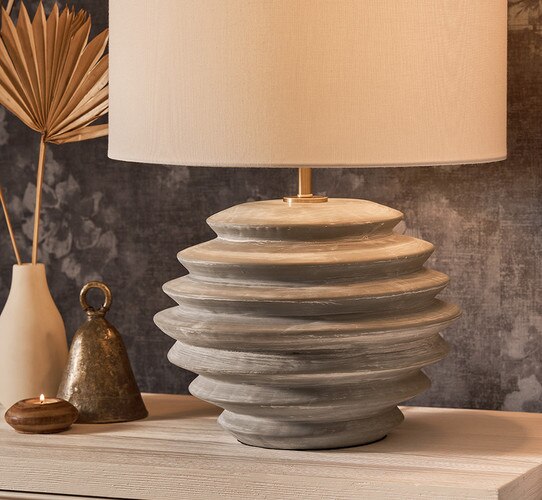 Ceramic lamp with textured finish next to a bell, candle, and vase on a wooden nightstand