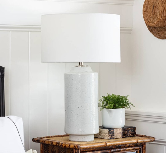 Tall gray ceramic table lamp next to a book and pot on a wooden side table