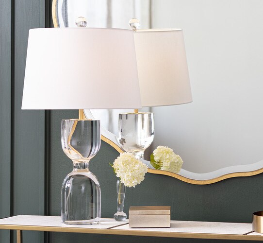 Hourglass shaped solid crystal table lamp on a white and gold console table