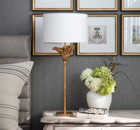 Thin gold table lamp with a flared top on a wooden side table