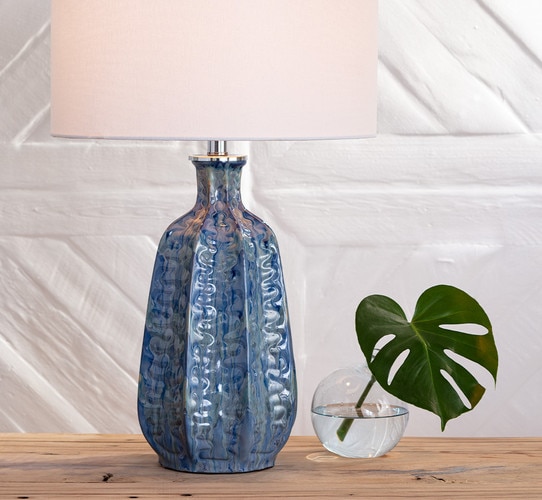 Textured blue table lamp next to a short vase with a green leaf in it