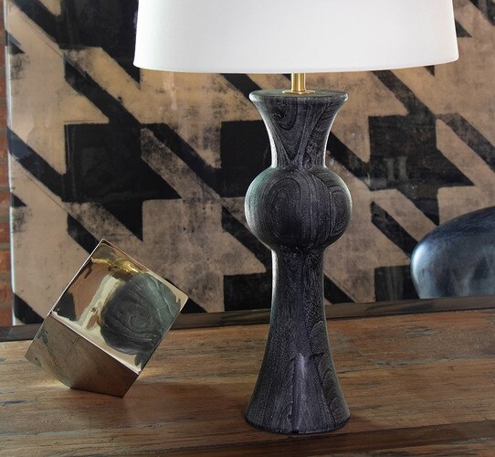 Glack wood table lamp next to a brass cube on a wooden console table
