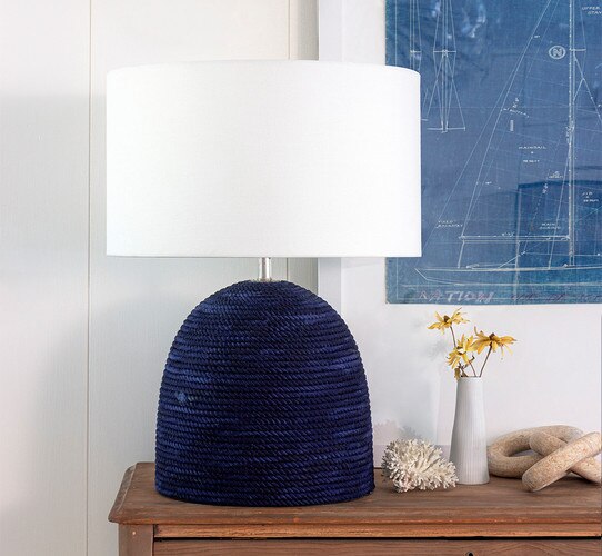 Blue rope lamp on a wooden console table next to marble chains and a piece of coral