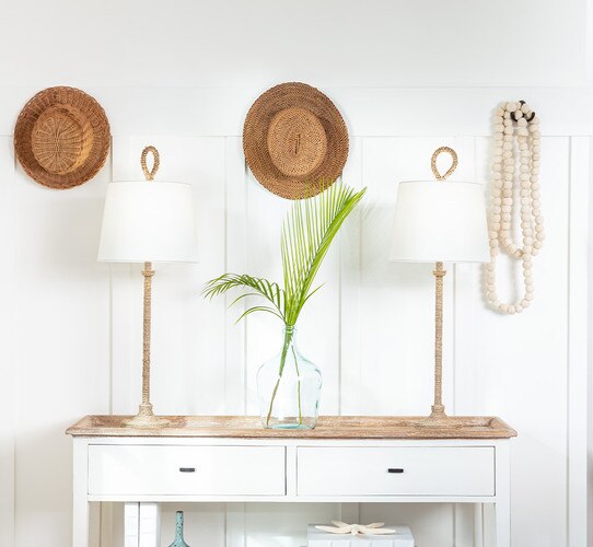 Rope buffet lamps flanking a clear vase with two palm leaves in it.