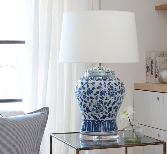 Ceramic painted white and blue table lamp on a side table next to a vase with a flower