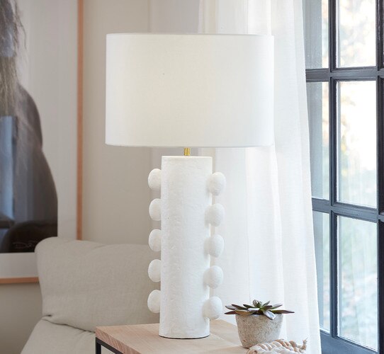 Modern white table lamp with nodules on the side of it next to a stone vase on a console table