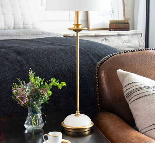 Traditional gold table lamp with alabaster base on a side table next to a vase of various puple and green flowers