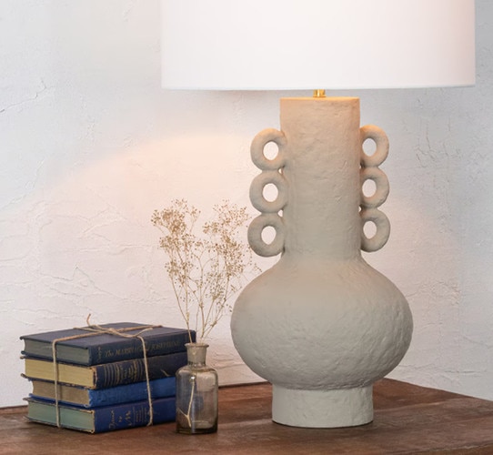 Brown textured table lamp with three rings on each side, next to four blue books wrapped with twine