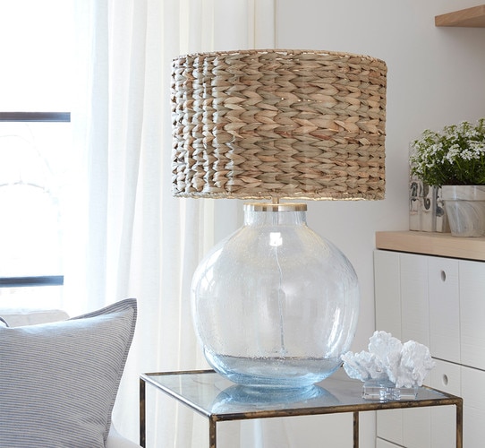 Clear glass table lamp with whicker shade on a gold side table