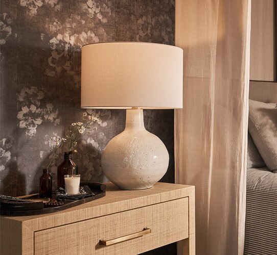 Circular white ceramic table lamp on a wooden nightstand beside a tray with flowers