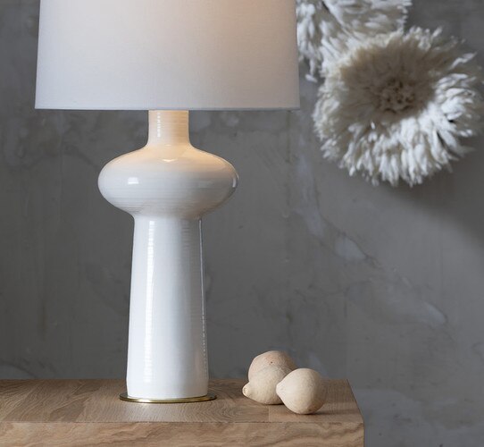 White ceramic table lamp with a disc atop the body on a wood side table