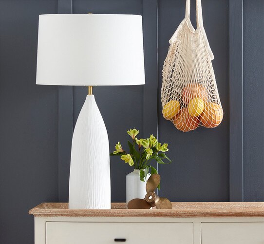 White textured table lamp beside a prop propellor and a white vase with yellow flowers