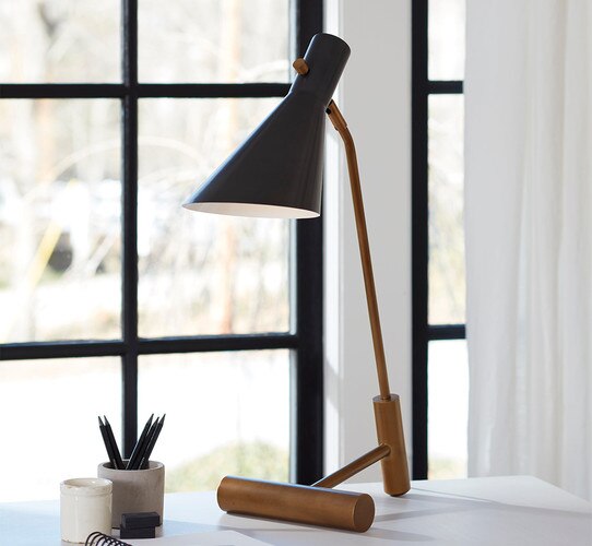 Brass and black task lamp on a white desk beside pens and a notebook