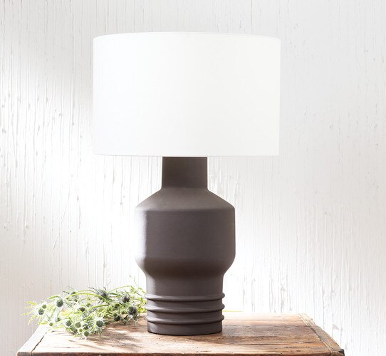 Brown modern ceramic table lamp on a wood side table next to a bundle of flowers