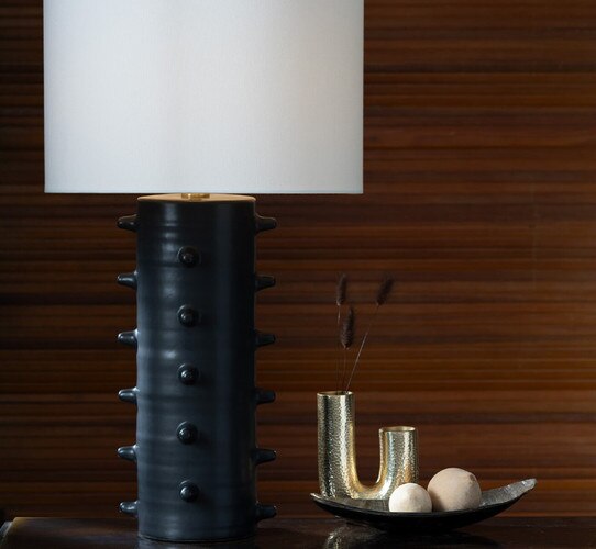 Black table lamp with spikes beside a metal bowl and brass candle holder