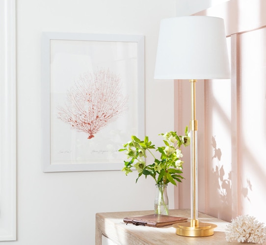 Gold buffet lamp with a clear glass body showing gold underneath on a side table in front of a pink wall