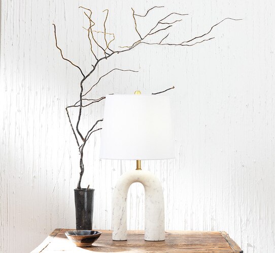 Marble arched table lamp on a wood table lamp next to a vase with a large branch