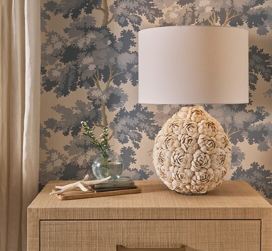 Table lamp with textured flower exterior made from shells on a nightstand next to a tray of decor