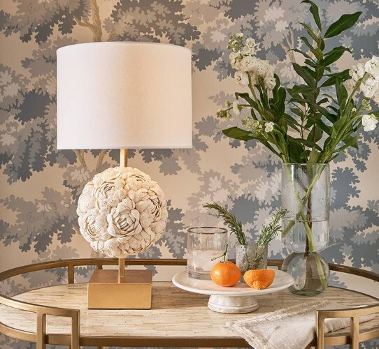 A Mini Shell lamp on a brass bar table next to flowers and oranges
