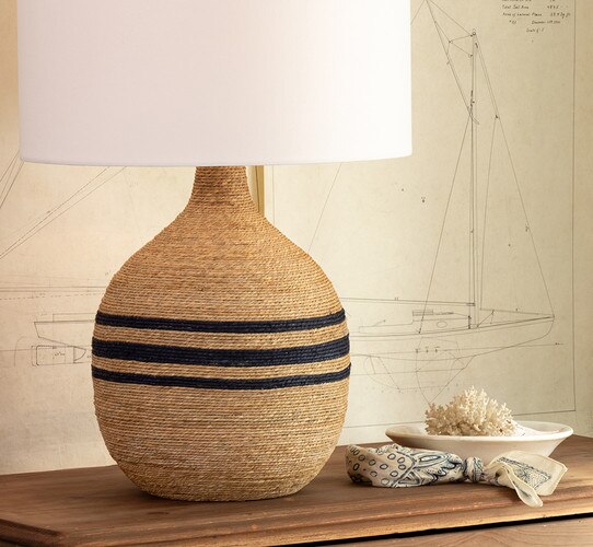 Rope table lamp with three bands of blue in the center on a wooden nightstand in front of a line drawing of a boat
