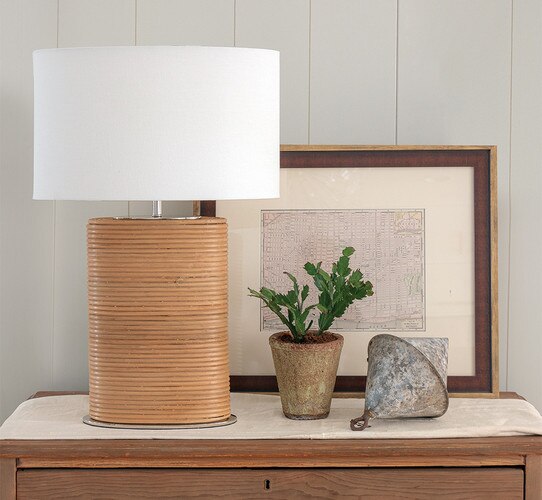 Drum rattan table lamp on a console table next to a stone vase