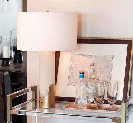 Alabaster table lamp with brass base on a bar cart with bottles of liquor