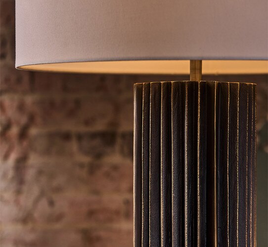 Black scalloped lamp with white shade in front of a brick wall