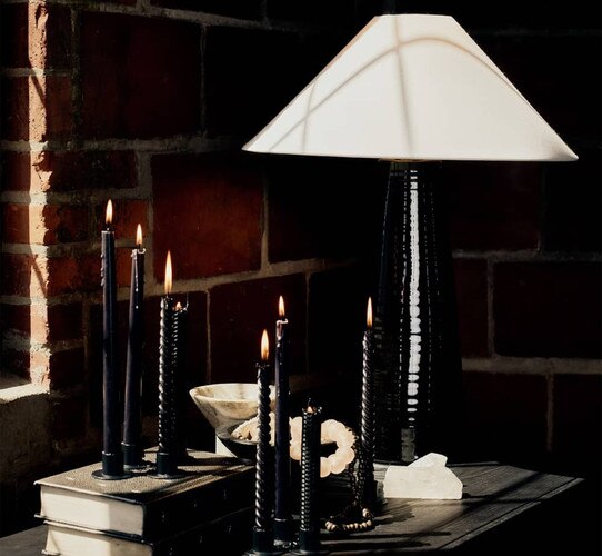 black lamp beside lit black candles beside a window