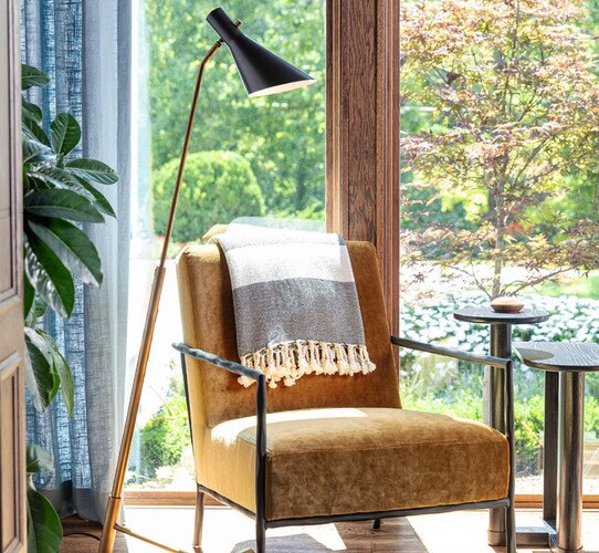 Brass and black lamp next to leather chair in front of large window