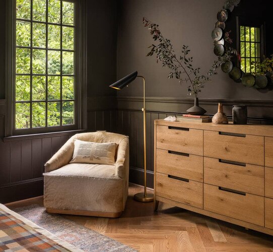 Black and brass floor lamp beside a dresser and accent chair near a window
