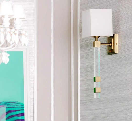 Brass and crystal wall sconce on a grey wall with a light green and purple painting in the background