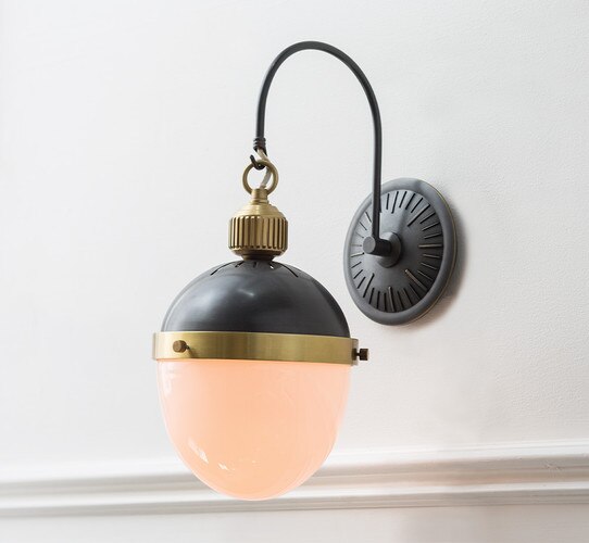 Black and brass sconce with milk glass on a white painted wall