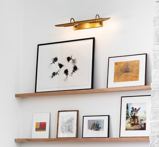 Large brass picture light above two thin wood shelves with photos